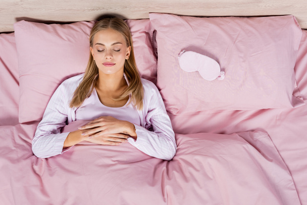 Vista superior de la mujer rubia durmiendo cerca de la máscara en la cama  - Foto, Imagen