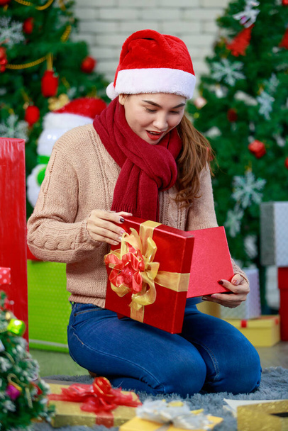 Kış kıyafeti giyen çekici Asyalı kadın ve Noel Baba 'nın şapkasıyla Noel' i neşeyle kutlayan hediyeler. Süslü Noel ağacı arka planı. Aile Noel partisi kavramı. - Fotoğraf, Görsel