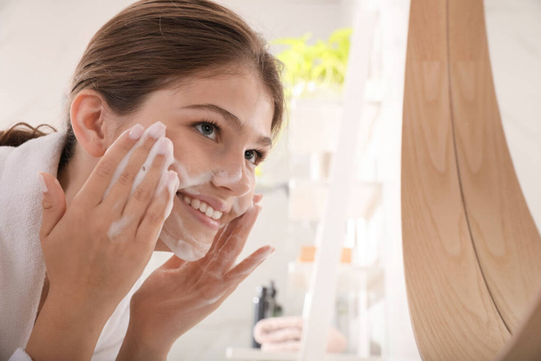 Beautiful teenage girl applying cleansing foam onto face in bathroom. Skin care cosmetic - Valokuva, kuva