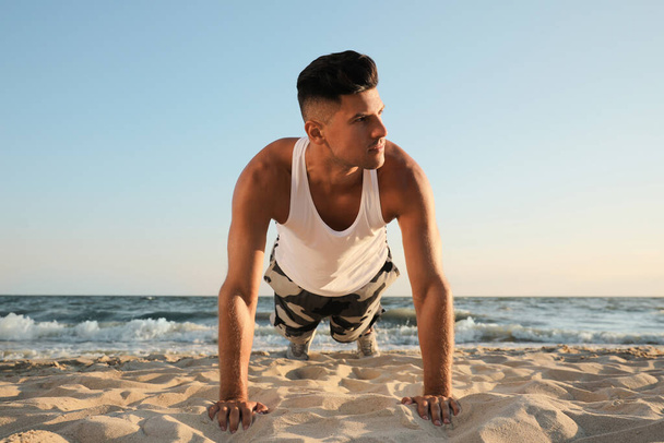 Sporty man doing plank on sandy beach - Foto, afbeelding