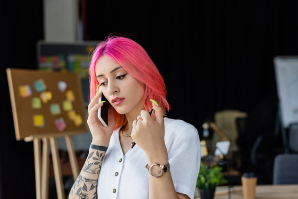 young businesswoman with pink hair talking on smartphone and holding pen - Photo, Image