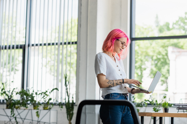 happy young businesswoman with pink hair using laptop in office - Photo, Image