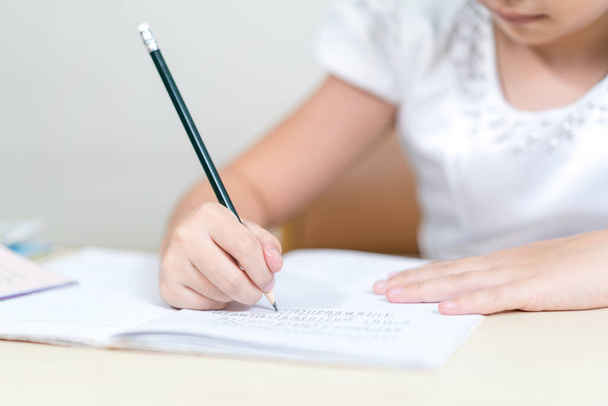A closeup shot of a little girl's hands writing in a copybook with a pencil - Fotó, kép