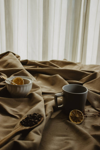 A vertical shot of roasted coffee beans on a ladle beside a cup and bowl with dried orange - Foto, Bild