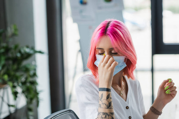 gerente tatuado com cabelo rosa ajustando máscara médica no escritório - Foto, Imagem