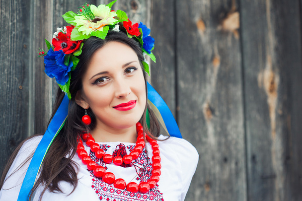Woman wearing national ukrainian clothes sitting in wooden hut - Valokuva, kuva