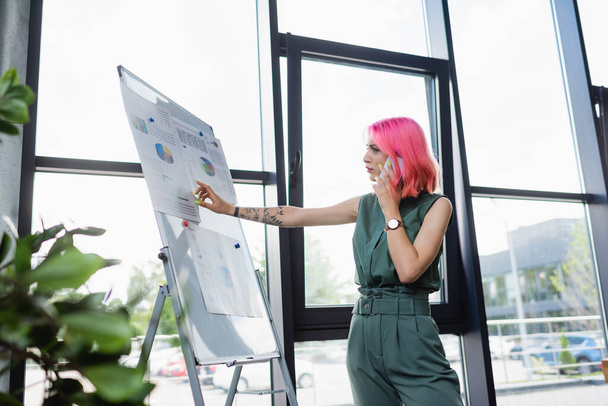 businesswoman with pink hair talking on cellphone while looking at flip chart with charts  - Fotoğraf, Görsel
