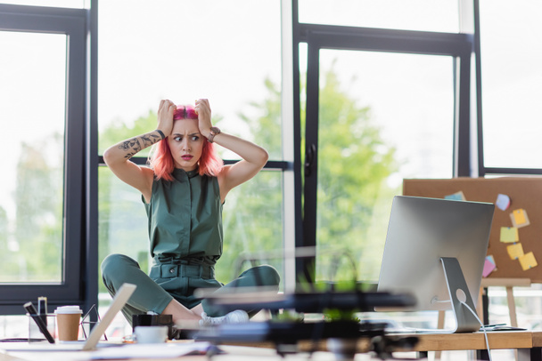 mujer de negocios estresada con el pelo rosa sentado con las piernas cruzadas en el escritorio en la oficina - Foto, Imagen