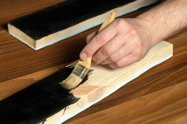 Wood plank restoration. Painting boards with black paint. Close-up of man hand holding a paint brush - Φωτογραφία, εικόνα