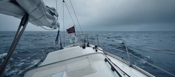Yacht sailing in a thunderstorm on a rainy autumn day. Top down view from the deck to the bow, mast and sails. Dramatic stormy sky, dark clouds. Norway - Photo, Image