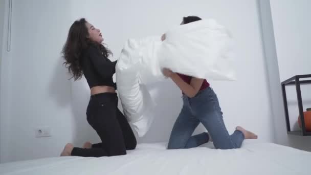 Két nő nevet, miközben párnacsata folyik az ágyon. közepes lövés - Felvétel, videó