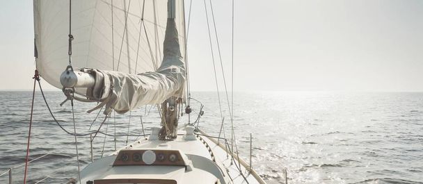 Bílá šalupa lanoví jachta plachtění na otevřeném moři při západu slunce. Jasná obloha. Pohled z paluby na příď, stěžeň, plachty. Doprava, cestování, plavba, sport, rekreace, volný čas, závodní, regata - Fotografie, Obrázek