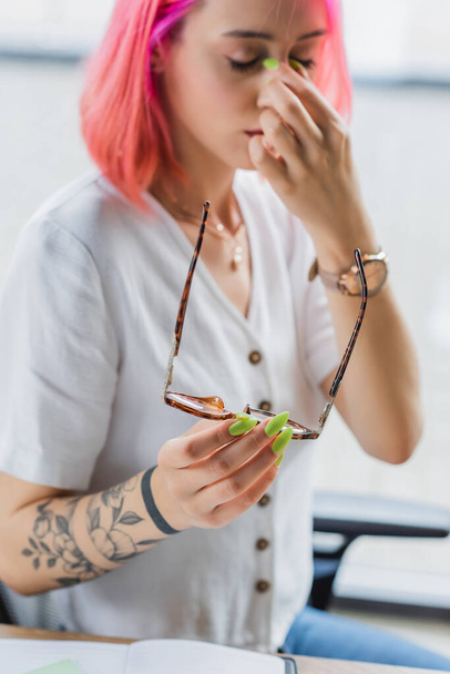 blurred and tired businesswoman with pink hair holding eyeglasses - Fotoğraf, Görsel