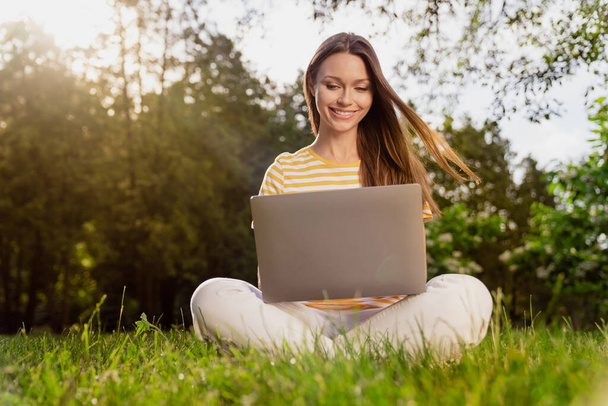 Full length body size photo woman sitting on grass using laptop working remotely in summer park - Fotó, kép