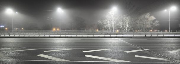 夜に霧の中で空の高速道路の照明。街路灯や道路標識を閉じるまで。暗い都市部のシーン、街並み。ラトビアのリガ。危険な運転,速度,自由,コンセプトイメージ - 写真・画像