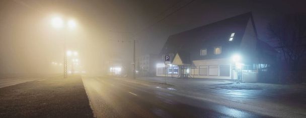 Пустой освещенный автомагистраль и закрытые магазины в тумане ночью. Дорожный знак крупным планом. Темная городская сцена, городской пейзаж. Рига, Латвия. Опасное вождение, концептуальный образ - Фото, изображение