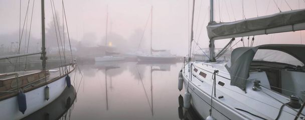 Парусные лодки пришвартованы к пирсу в густом белом утреннем тумане на рассвете, крупным планом. Яхт клуб в Киле, Германия. Спорт, отдых, транспорт - Фото, изображение