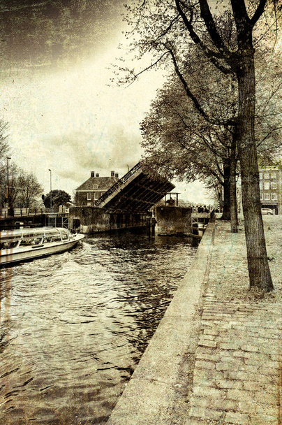 Turistická loď na kanálu Amsterdam v historickém centru města. Amsterodamský padací most je v polootevřené poloze, zatímco kolem projíždí vodní autobus. Tónovaný obrázek ve stylu ročníku - Fotografie, Obrázek