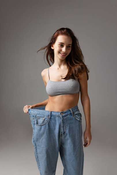 Portrait of young beautiful slim girl in blue jeans jumpersuit posing isolated over gray studio background. Weight Loss concept. - Zdjęcie, obraz