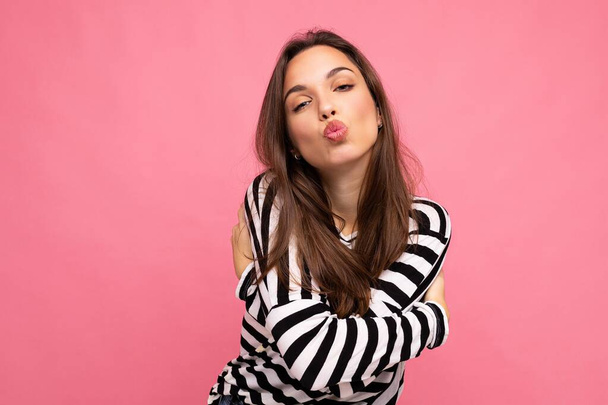 Photo shot of cute attractive pretty young brunette woman wearing casual striped longsleeve isolated over colorful background with copy space and giving kiss - Fotoğraf, Görsel