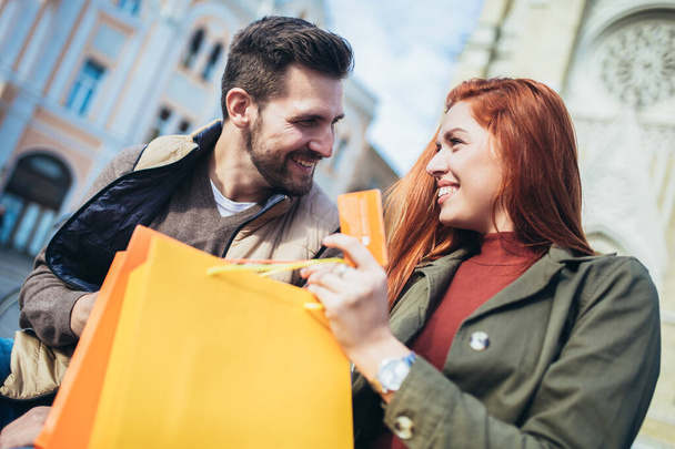 Retrato de pareja feliz con bolsas de compras después de comprar en la ciudad sonriendo y sosteniendo la tarjeta de crédito
 - Foto, imagen