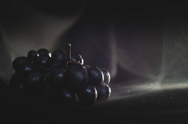 A branch of ripe grapes on a dark background with splashes of water. Space for text - Foto, Bild