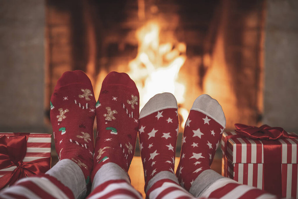 Couple in Christmas socks near fireplace. Man and woman having fun together. People relaxing at home. Winter holiday Xmas and New Year concept - Photo, image