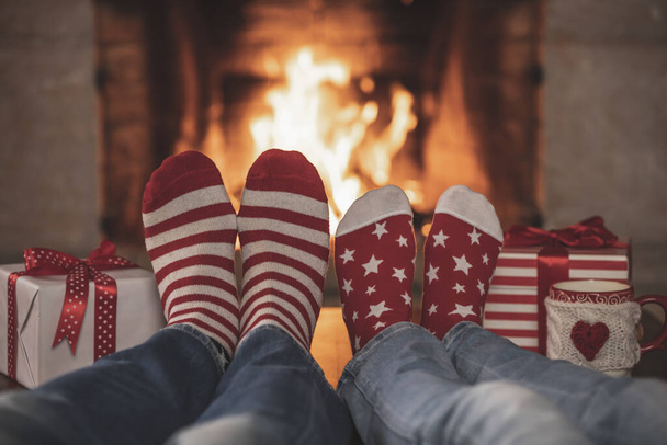 Couple in Christmas socks near fireplace. Man and woman having fun together. People relaxing at home. Winter holiday Xmas and New Year concept - Φωτογραφία, εικόνα