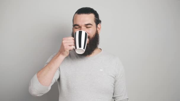 Felvételek fiatal vidám szakállas férfi ivás csésze kávét szürke háttér - Felvétel, videó