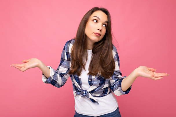 Portret foto van jonge attente mooie brunette vrouw met oprechte emoties dragen stijlvolle check shirt geïsoleerd op roze achtergrond met kopieerruimte en met twijfels. - Foto, afbeelding