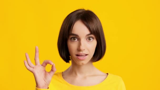 Radosna młoda dama Gesturing i mówiąc OK na żółtym tle - Materiał filmowy, wideo