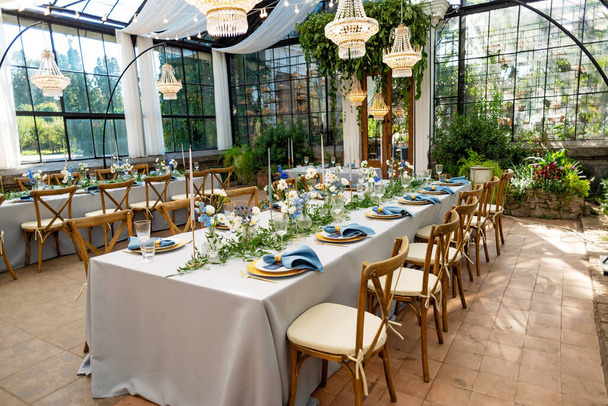 Hodovní svatební stůl s modrými ubrousky, zlatými příbory, křišťálem, čerstvými květinami a svíčkami. Svatební dekorace. Měkké selektivní zaměření. - Fotografie, Obrázek