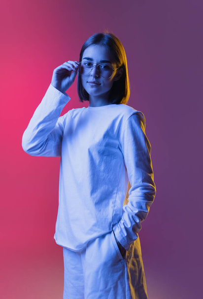 Close-up portrait of young cute girl, student in casual clothes listening to music isolated on pink-purple studio backgroud in neon. - Φωτογραφία, εικόνα