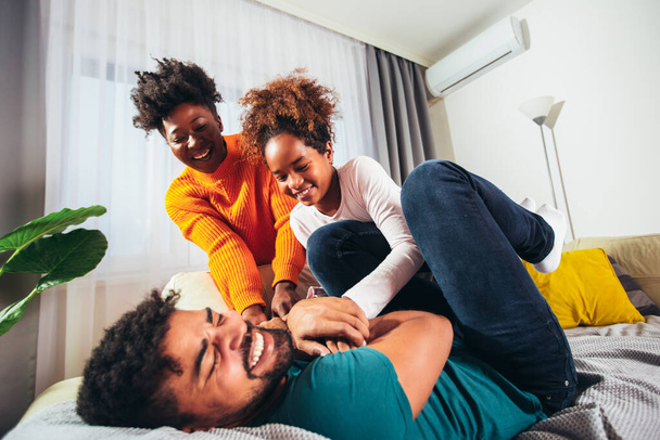 Χαριτωμένη αφροαμερικανική οικογένεια απολαμβάνοντας το χρόνο μαζί στο σπίτι διασκεδάζοντας. - Φωτογραφία, εικόνα