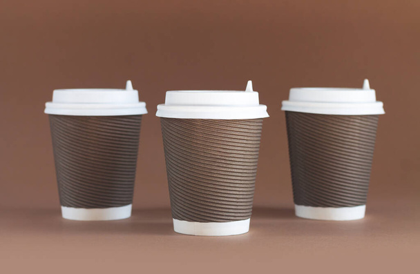 Tres tazas de café biodegradables de papel con tapas sobre fondo marrón con espacio para copiar - Foto, Imagen