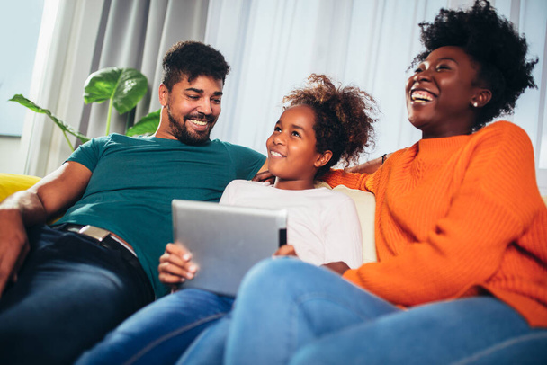 Szczęśliwa afrykańska rodzina bawiąca się cyfrowym tabletem w domu. - Zdjęcie, obraz