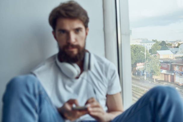 ヘッドフォンで窓の近くに座ってヘッドフォンで音楽を聴いている髭の男 - 写真・画像