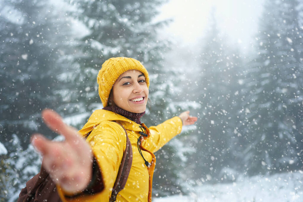 Happy joyful woman at winter forest with falling snow. Outdoor Christmas vacation - 写真・画像