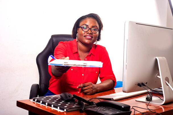 une charmante femme d'affaires en lunettes assise au bureau donnant un document à quelqu'un souriant. - Photo, image