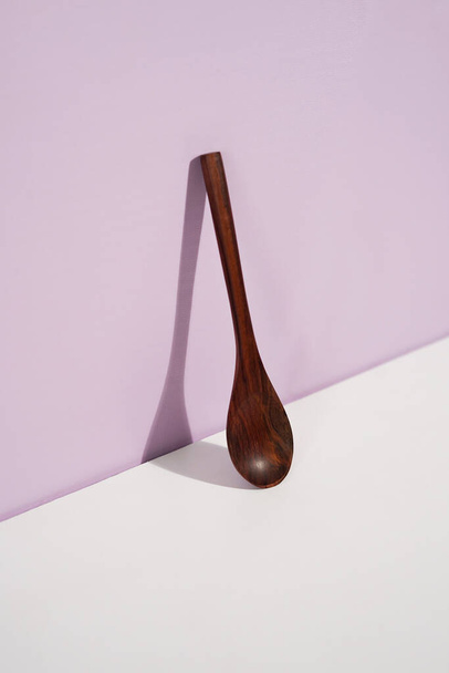 a wooden spoon standing on the lavender wall. a studio shot of the organic utensils. suitable for advertisement. - Foto, Bild