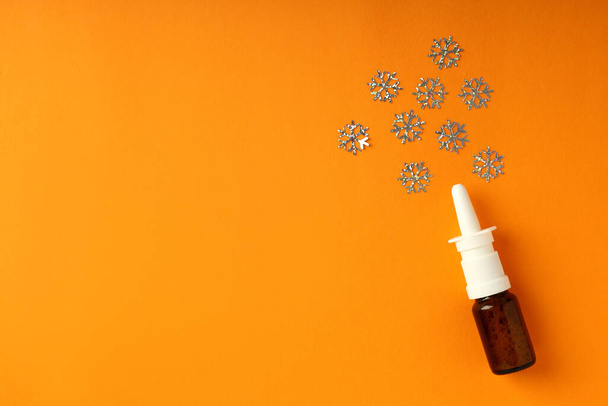 Prázdná láhev nosní sprej a dekorativní sněhové vločky na oranžovém pozadí - Fotografie, Obrázek