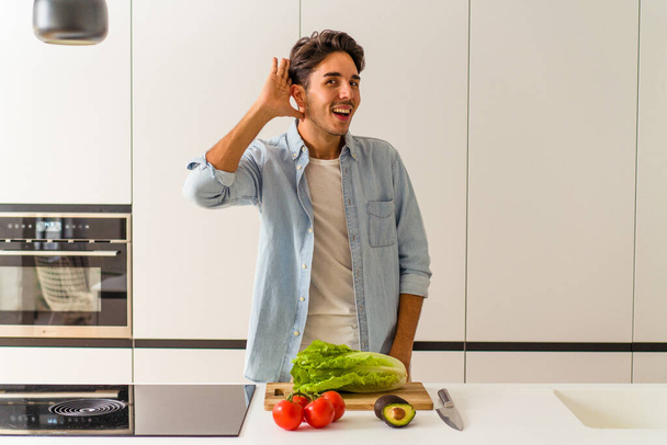 Young mixed race man preparing a salad for lunch trying to listening a gossip. - Photo, Image