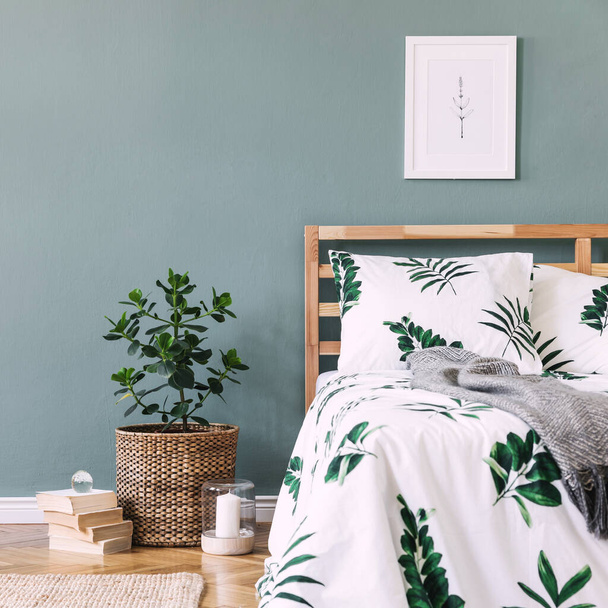 Creative composition of cozy and stylish bedroom with mock up poster frame, bed, white bedclothes with green leaves, carpet, wooden cube as coffee table and boho accessories. Eucalyptus wall and parquet floor. Template - Foto, Imagem