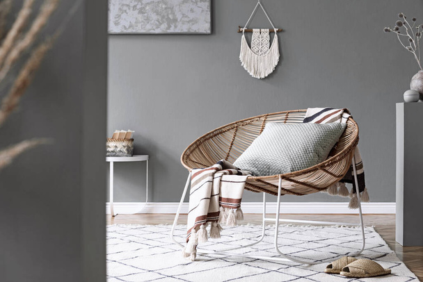 Stylish composition of creative and cozy living room interior with coffee table, rattan armchair, plants, carpet and beautiful boho accessories. Grey walls and parquet floor. - Foto, Imagem