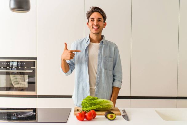 Jeune homme métis préparant une salade pour le déjeuner personne pointant à la main vers un espace de copie de chemise, fier et confiant - Photo, image