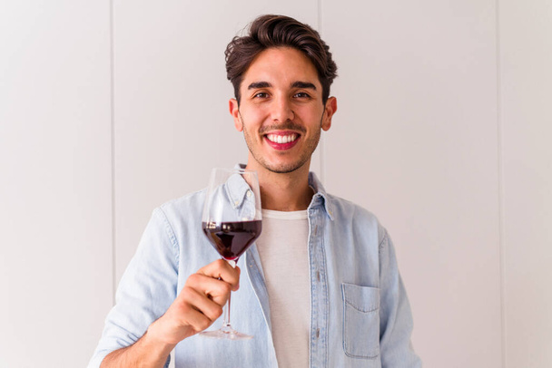 Young mixed race man drinking wine in a kitchen - Fotó, kép