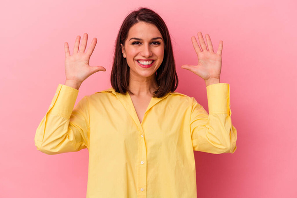 Young caucasian woman isolated on pink background showing number ten with hands. - Fotó, kép