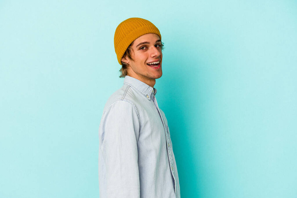 Young caucasian man with make up isolated on blue background  confident keeping hands on hips. - Foto, afbeelding