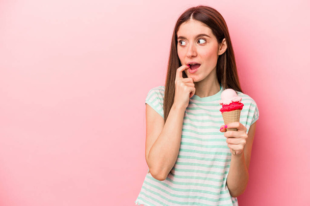 Jeune femme caucasienne tenant une crème glacée isolée sur fond rose détendu penser à quelque chose qui regarde un espace de copie. - Photo, image