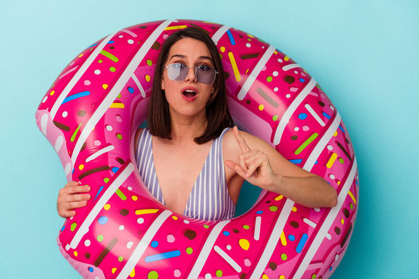 Young caucasian woman with inflatable donut isolated on blue background having an idea, inspiration concept. - Photo, Image